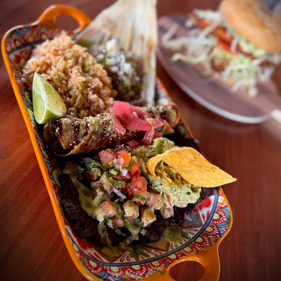 Colorful platter of Mexican food with rice, tamale, taquitos, guacamole, salsa, and a lime wedge.