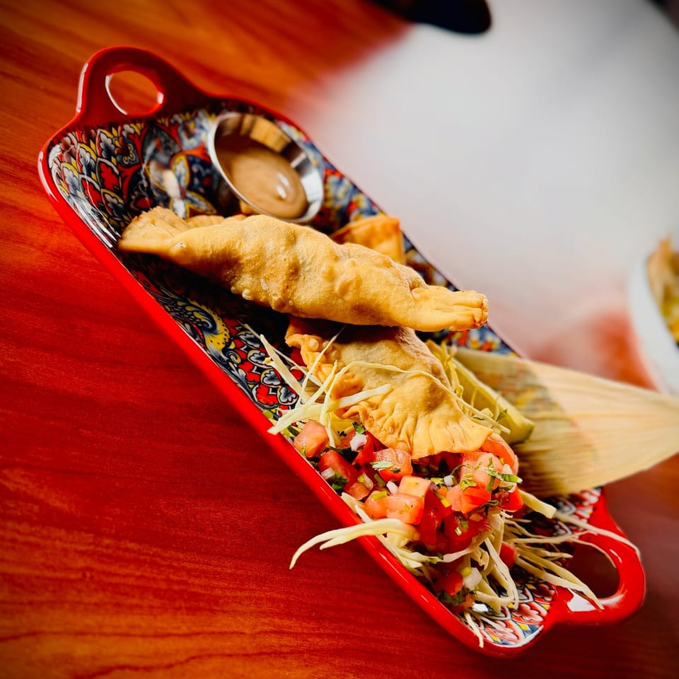 Fried empanadas with shredded cabbage and pico de gallo, served on a colorful patterned tray.