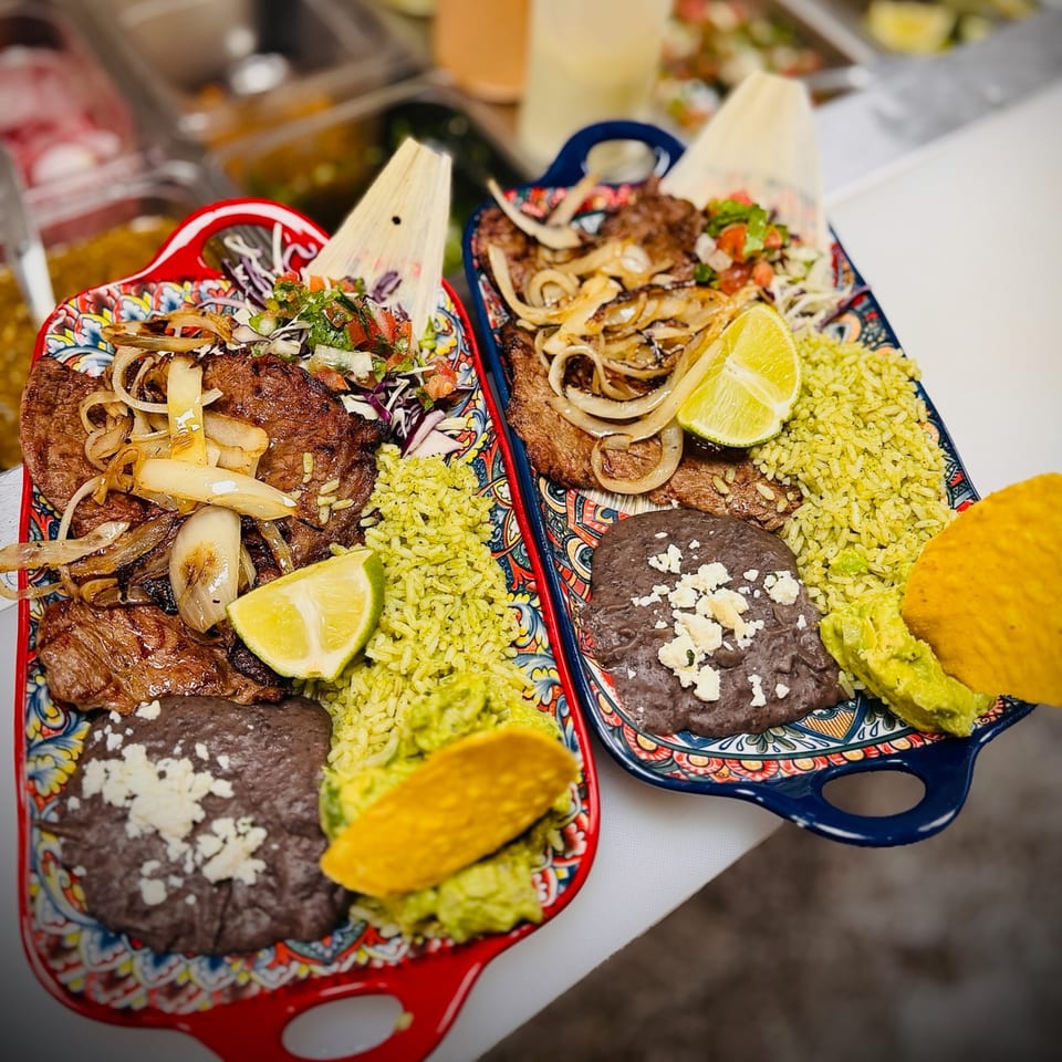Two colorful plates of steak with onions, green rice, black beans, guacamole, and lime.