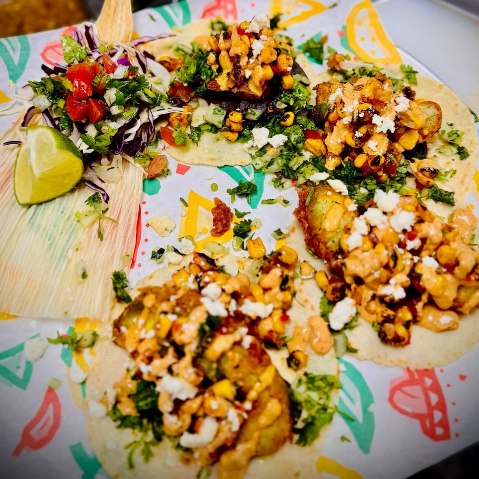 Four colorful tacos with various toppings, including corn, cheese, and fresh salsa, on a patterned paper.