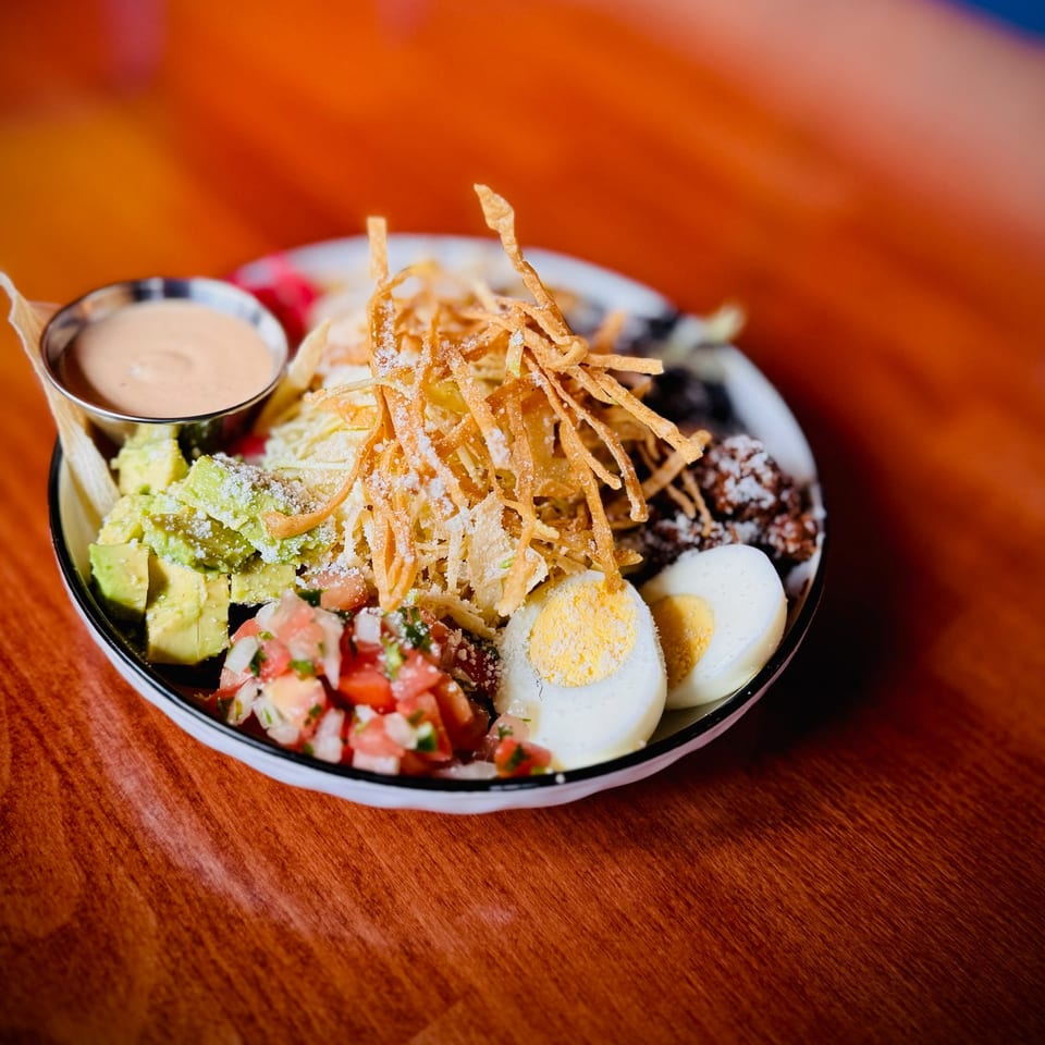 A colorful salad with avocado, pico de gallo, hard-boiled eggs, and crispy tortilla strips.