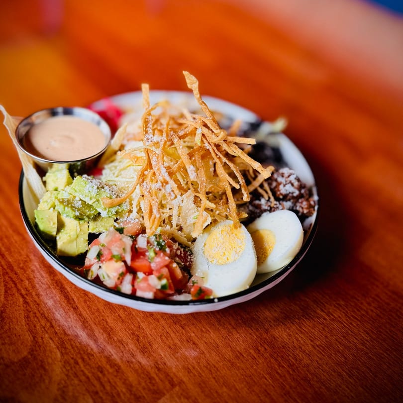 A colorful salad with avocado, pico de gallo, hard-boiled eggs, and crispy tortilla strips.